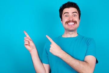 young handsome Caucasian man with moustache wearing blue t-shirt against blue background points at copy space indicates for advertising gives right direction