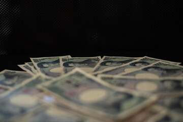 Blurred focus of pile of Japanese money in 1000 yen bills and 10000 yen bills on black background in soft focus