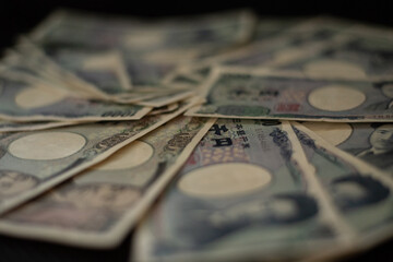 Blurred focus of pile of Japanese money in 1000 yen bills and 10000 yen bills on black background in soft focus