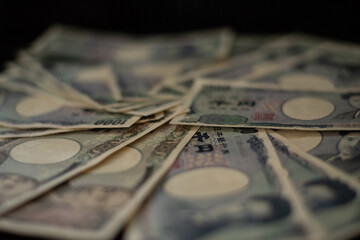 Blurred focus of pile of Japanese money in 1000 yen bills and 10000 yen bills on black background in soft focus