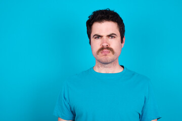 Fototapeta premium young handsome Caucasian man with moustache wearing blue t-shirt against blue background Pointing down with fingers showing advertisement, surprised face and open mouth