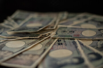 Blurred focus of pile of Japanese money in 1000 yen bills and 10000 yen bills on black background in soft focus