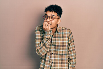 Young african american man wearing casual clothes and glasses looking stressed and nervous with hands on mouth biting nails. anxiety problem.