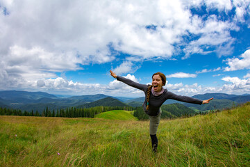 Smiling young girl tourist in the mountains. Young woman tourist in the mountains on the background of blue sky with white clouds. Beautiful mountain landscape view