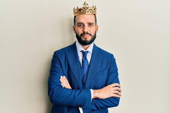 Young business man with beard wearing king crown relaxed with serious expression on face. simple and natural looking at the camera.