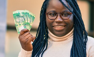 Young african american woman smiling happy holding south africa rands banknotes at the city.