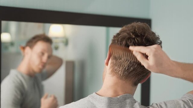 Portrait in the mirror of a young man combing his hair with a wooden comb