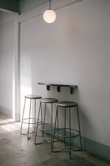 a loft white wall room with three silver steel chairs, a silver steel table and a round pendant lamp in bright light and shadow corner 