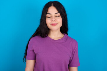 young beautiful tattooed girl wearing blue t-shirt standing against blue background nice-looking sweet charming cute attractive lovely winsome sweet peaceful closed eyes