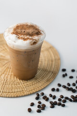 a glass of cappuccino coffee with sprinkled chocolate on milk foam sitting on rattan tray and coffee beans on the side