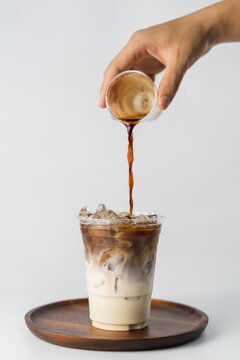 pouring espresso shot coffee into a glass of milk to become an iced latte on the wooden plate