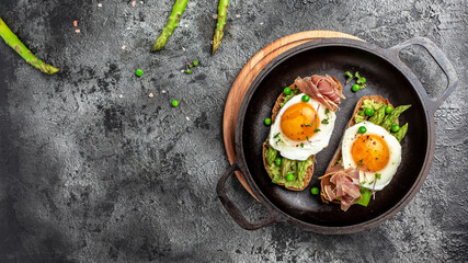 Breakfast with asparagus, egg, bacon and toast on dark background. Long banner format, top view