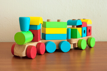 Stacking Train Toddler Toy for little children, on reflective wooden floor, next to the wall. Baby train made of wooden geometric blocks. Colorful wooden stacking train for kids. Shot in kid's room.