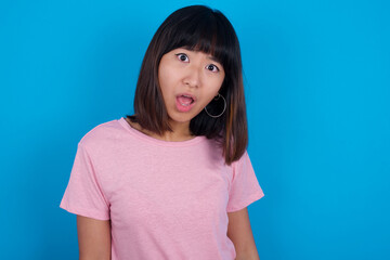 Expressive facial expressions. Shocked stupefied young beautiful asian woman wearing pink t-shirt against blue wall, keeps jaw dropped feels stunned from what he sees aside.