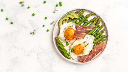 Green asparagus with fried egg, avocado and prosciutto on the plate. ketogenic diet lunch concept. menu, top view