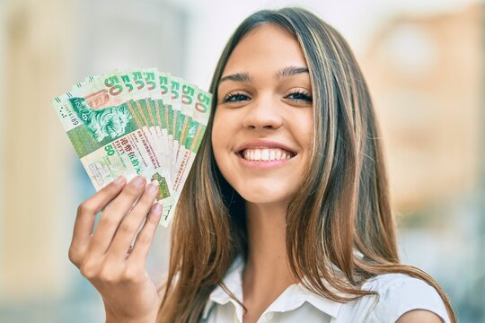 Beautiful latin teenager girl smiling happy holding hong kong dollars at the city.