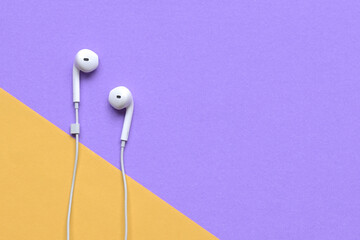 White ear phones on purple and yellow background. Top view with copy space.