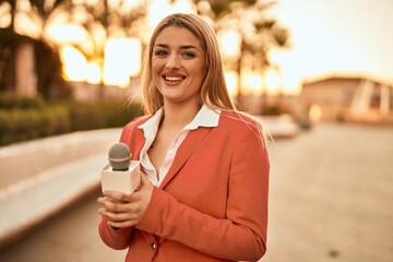 Young blonde reporter woman working using microphone at the city.