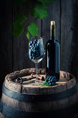 Red wine in bottle and a glass on wooden barrel.