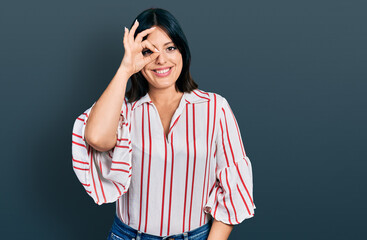 Young hispanic girl wearing casual clothes doing ok gesture with hand smiling, eye looking through fingers with happy face.