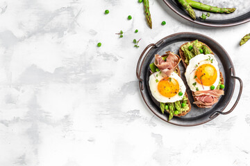 healthy breakfast toasts with avocado, asparagus, jamon, ham, prosciutto and fried egg on wtite plate. Long banner format, top view