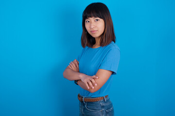 Fototapeta na wymiar Portrait of young beautiful asian girl wearing blue t-shirt against blue background standing with folded arms and smiling