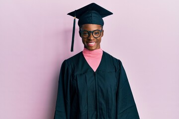 Young african american girl wearing graduation cap and ceremony robe with a happy and cool smile on...
