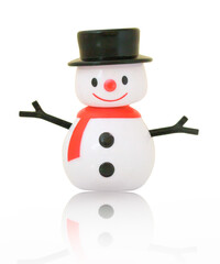 Small plastic snowman toy. Isolated on white background with shadow reflection. Snowman with black hat, eyes, twigs and buttons. Red nose and scarf. Lovely simply snowman doll, closeup shot.