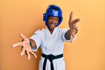 Young african american girl wearing taekwondo kimono and protection helmet looking at the camera...