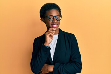 Young african american girl wearing business jacket and glasses smiling looking confident at the camera with crossed arms and hand on chin. thinking positive.