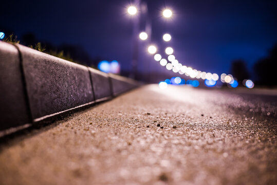 Rainy night in the big city, the empty highway with lanterns. Close up view of a level curb on the road