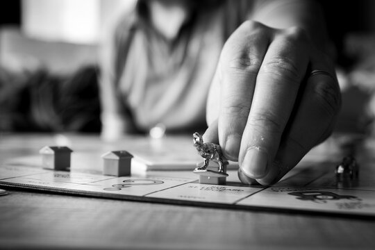 Brecht, Belgium - 28 July 2020: The Fingers Of A Hand Of A Person Reaching Out Holding The Metal Dinosaur Pawn Or Game Piece Of A Game Of Monopoly And Placing It On A Playing Field Of The Game Board.