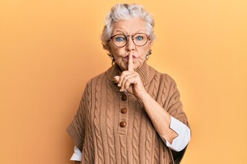 Senior grey-haired woman wearing casual clothes and glasses asking to be quiet with finger on lips....