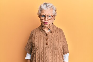 Senior grey-haired woman wearing casual clothes and glasses making fish face with lips, crazy and...