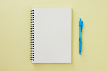 Spiral Notebook or Spring Notebook in Unlined Type and Blue Pen on Pastel Yellow Minimalist Background. Spiral Notebook Mock up on Center Frame