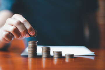 Closeup man hands. Businessman holding coin to place on stack of coins placed on the table....