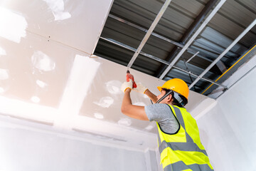 Construction workers using an electric drill are install the ceiling house at construction site, Ceiling installation ideas - obrazy, fototapety, plakaty
