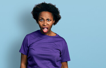 Fototapeta na wymiar African american woman with afro hair wearing casual purple t shirt in shock face, looking skeptical and sarcastic, surprised with open mouth