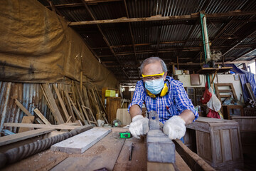Naklejka na ściany i meble Elderly carpenter man wear protective mask and headphone working using spokeshave ​for wood polishing. factory industry woodwork