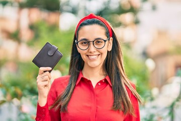 Fototapeta na wymiar Young hispanic woman smiling happy holding leather wallet at the city.