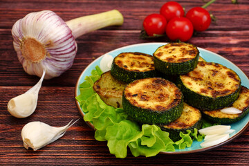Fried zucchini with garlic and tomatoes on a wooden table