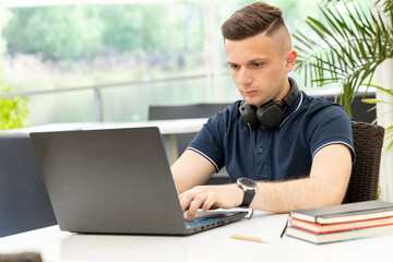 Young man writes text in a laptop while sitting at a table in a co working cafe. Male freelancer...