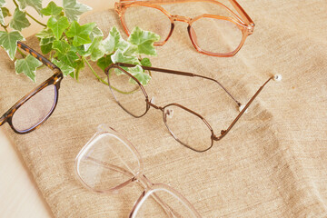 stylish eye glasses and plant leaves on linen fabric, brown background