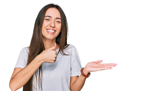 Young hispanic girl wearing casual white t shirt showing palm hand and doing ok gesture with thumbs up, smiling happy and cheerful