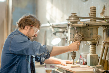 Craftsman uses drilling machine to make a hole on wooden plank