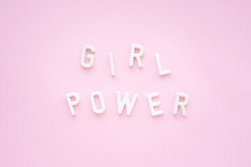 Inscription: girl power from white plaster letters on a pink background. Feminist slogan.