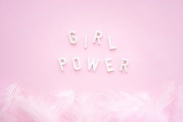 Inscription: girl power from white plaster letters on a pink background with feathers. Feminism slogan.