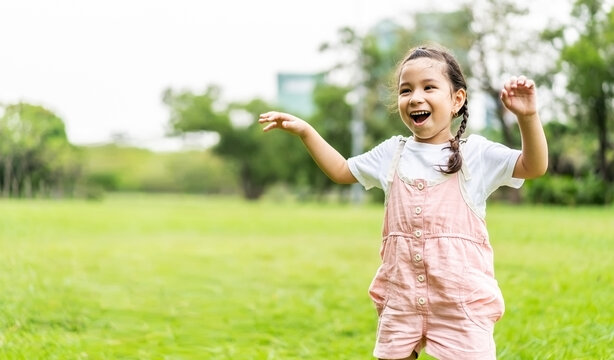 Portrait of happy pretty child girl smiling and raises her hand while standing in the park, ​Positive female kid enjoying warm day in fall park