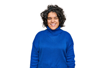 Young hispanic woman with curly hair wearing turtleneck sweater winking looking at the camera with...