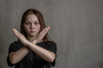 Tear-stained girl teenage girl shows stop gesture with crossed hands. Empty space for text